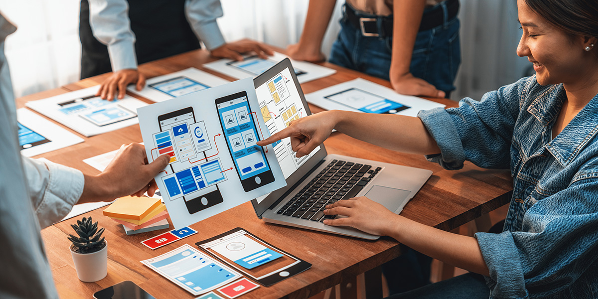 front-end developer team brainstorming UI and UX designs for mobile app on paper wireframe interface. User interface development team