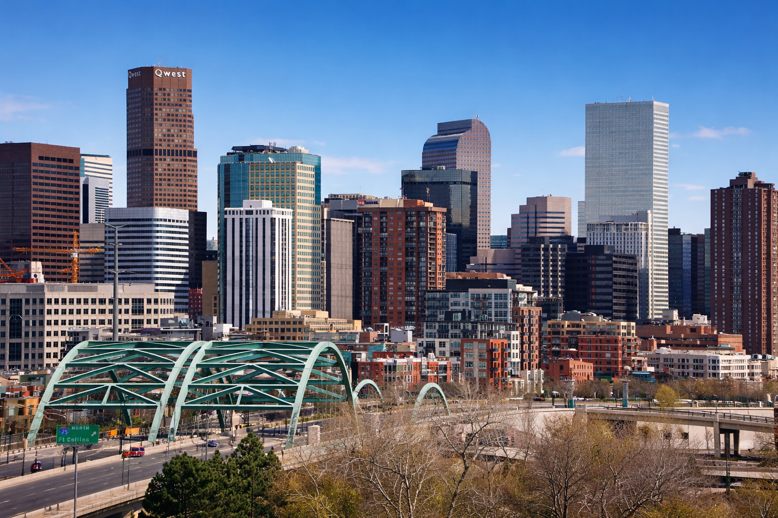 Photorealistic daytime view of the downtown Denver skyline with modern skyscrapers under a clear blue sky, a green arched bridge crossing a highway in the foreground, and mixed residential and commercial buildings throughout the city.